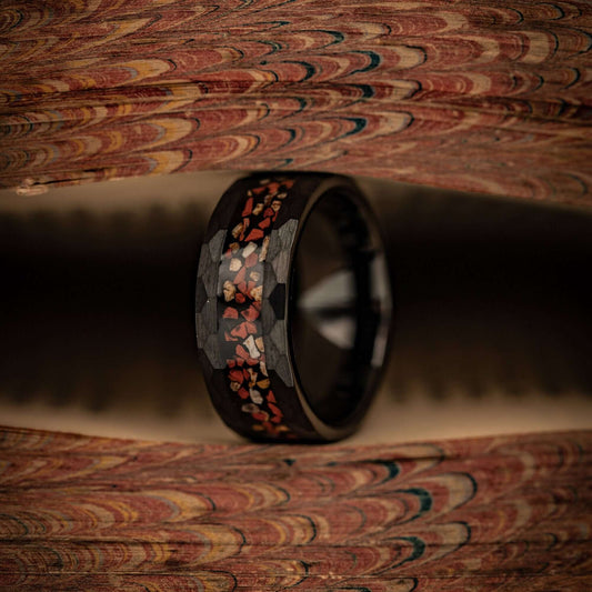 Hammered Black Tungsten Wedding Ring with Red and White Dinosaur Bone Inlay standing on its side between pages of a book