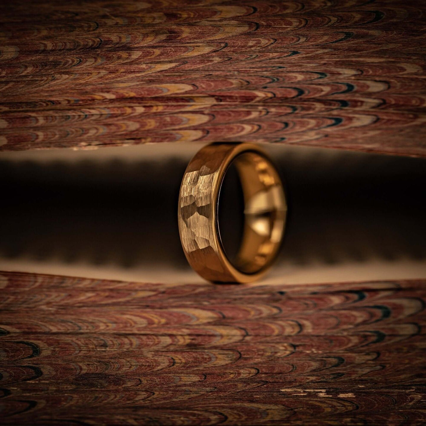 Women's 4mm Hammered Yellow Gold Tungsten Wedding Ring standing on its side between pages of a book