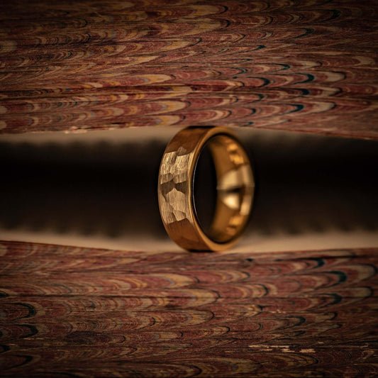 Women's 4mm Hammered Yellow Gold Tungsten Wedding Ring standing on its side between pages of a book