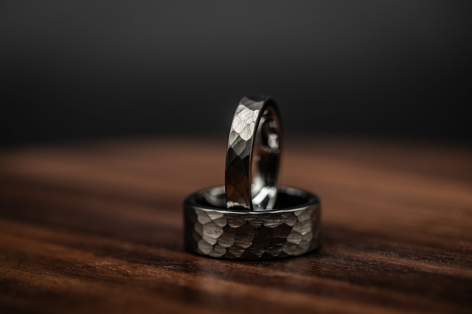 Two hammered tungsten rings showcasing a bold, rustic design on a wooden surface, highlighting unique craftsmanship.