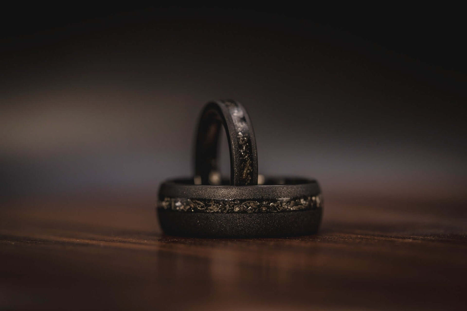 Unique handcrafted couples ring sets with black meteorite inlay on wooden surface, perfect for wedding or engagement.
