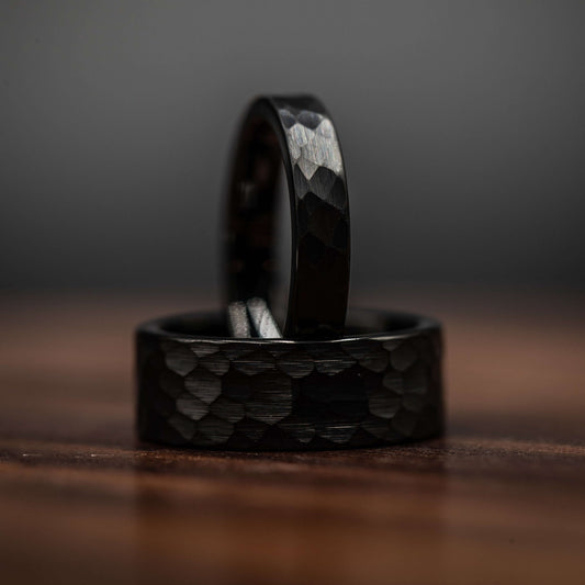 Black hammered tungsten wedding rings set on a wooden surface, showcasing bold and rustic design for couples.