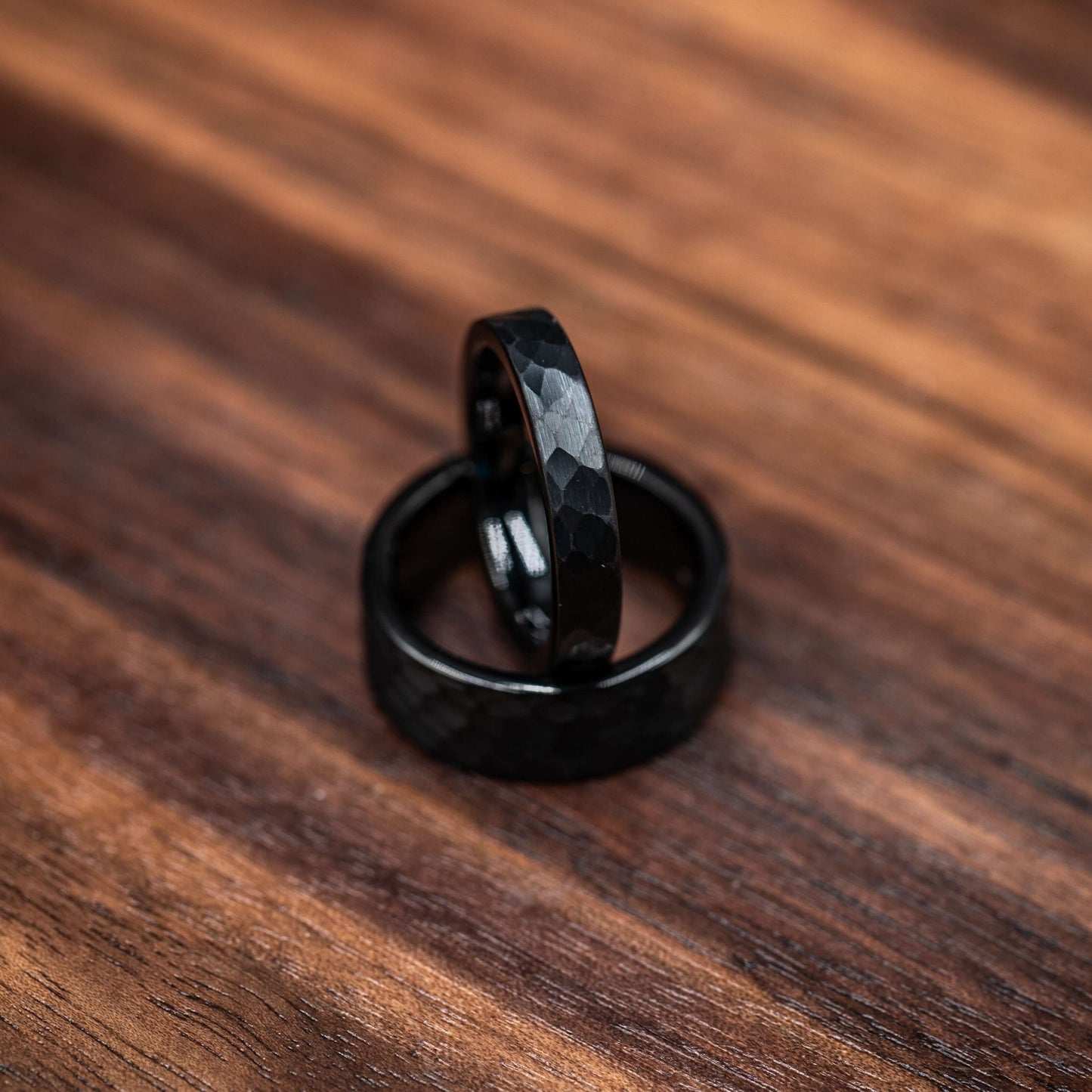 Two black hammered tungsten wedding rings on a wooden surface, showcasing their bold and rustic design.