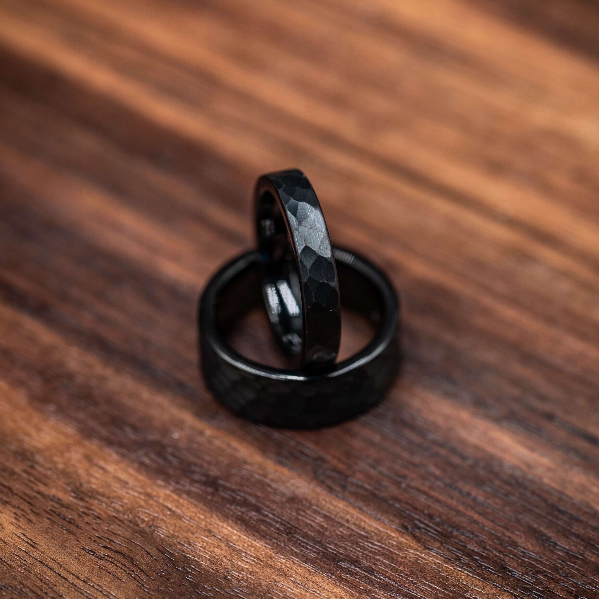 Two black hammered tungsten wedding rings on a wooden surface, showcasing their bold and rustic design.