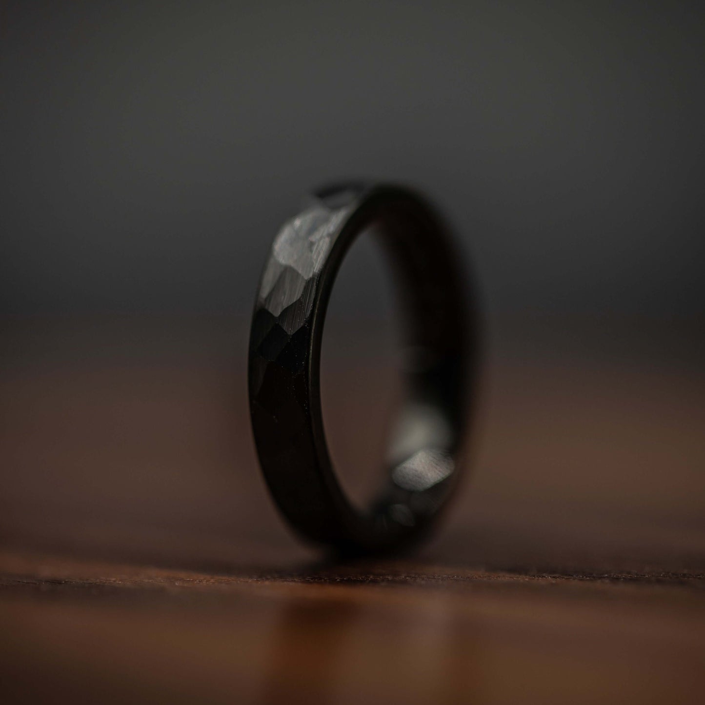 Hammered black tungsten wedding ring displayed on wooden surface, showcasing unique texture and durability.