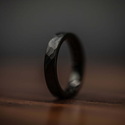 Hammered black tungsten wedding ring displayed on wooden surface, showcasing unique texture and durability.