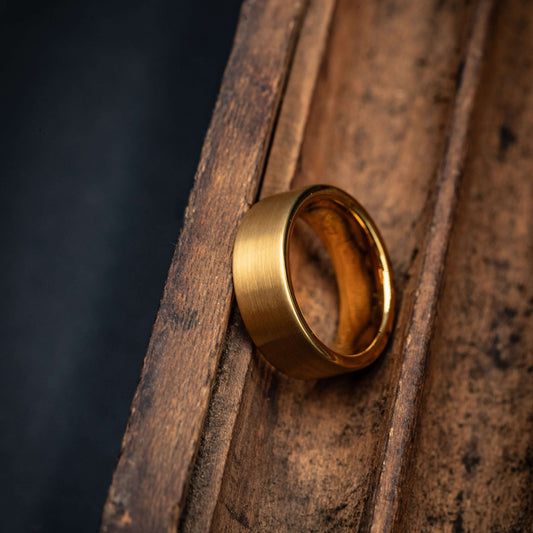 Gold brushed tungsten wedding band resting on a rustic wooden surface, showcasing its unique finish and design.