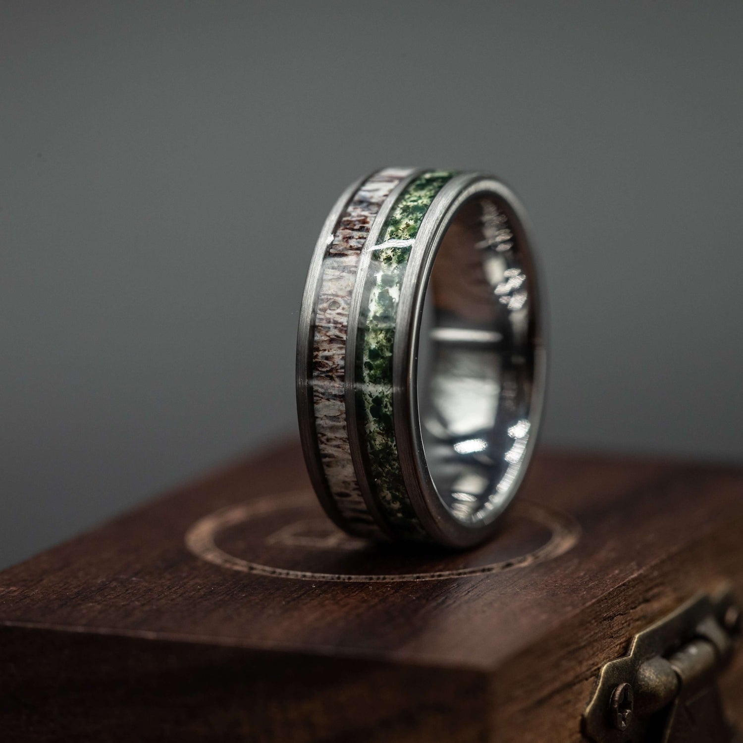 Mens deer antler and moss agate wedding band on a wooden display, showcasing polished silver tungsten and natural textures.