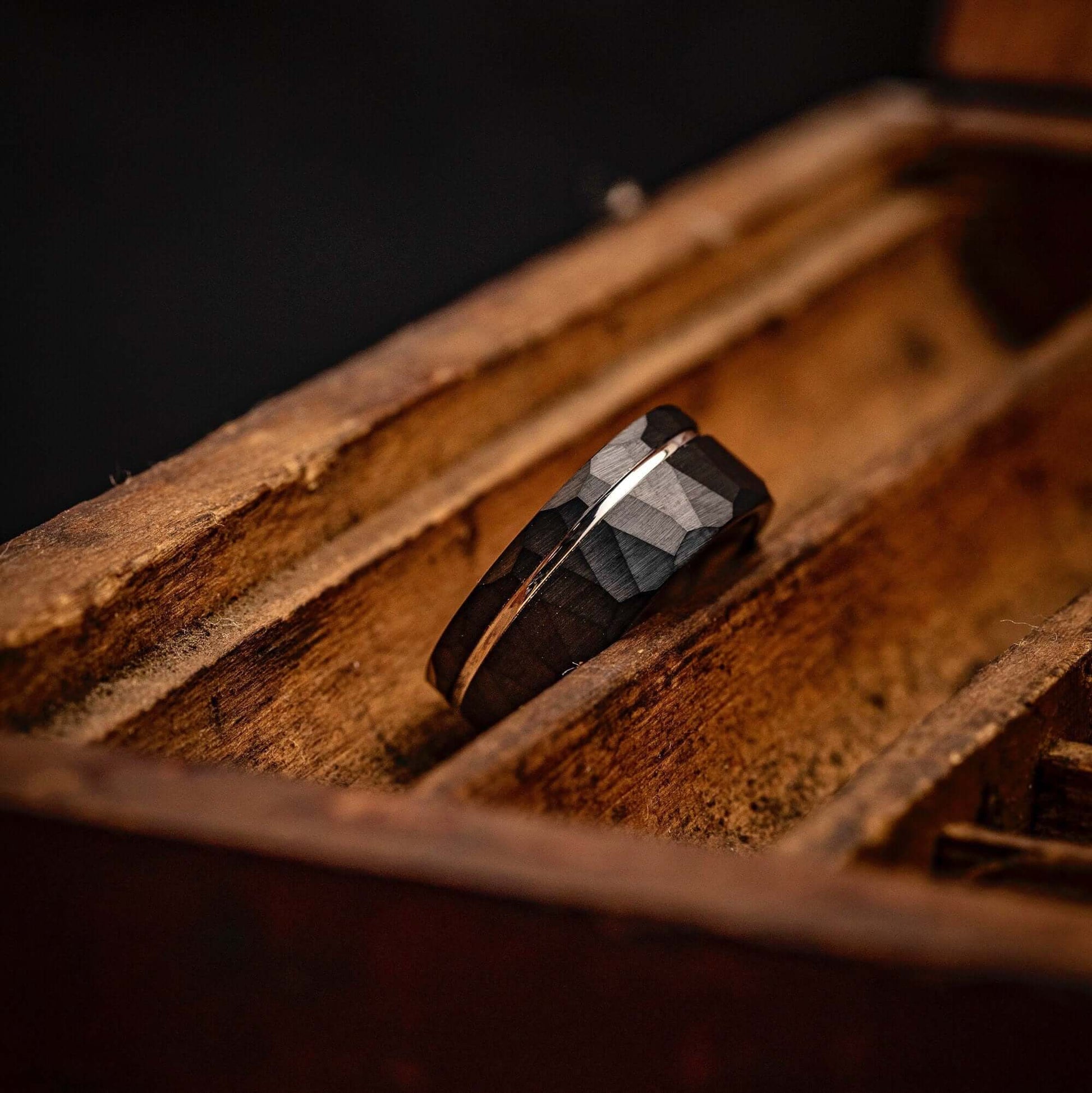 Hammered Black Tungsten Wedding Band with Silver Channel Inlay and Polished Silver Inner Band leaning on its side in old wooden box