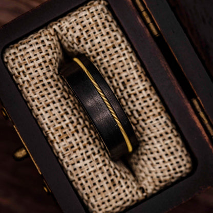 Black tungsten wedding band with Guitar String inlay inside walnut ring box between burlap cushions