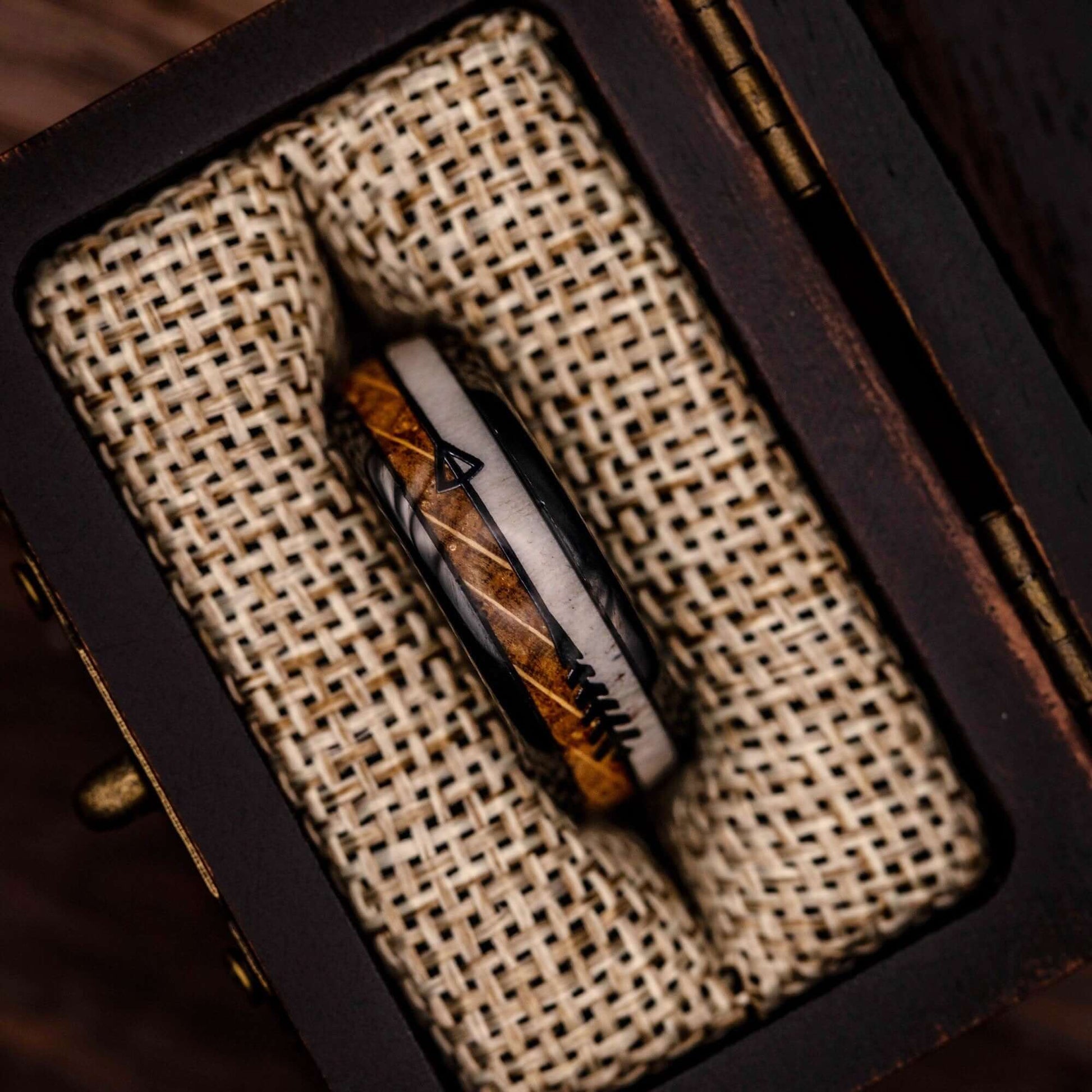 Men's 8mm wedding band with whiskey barrel and deer antler inlay inside a walnut ring box between burlap cushions