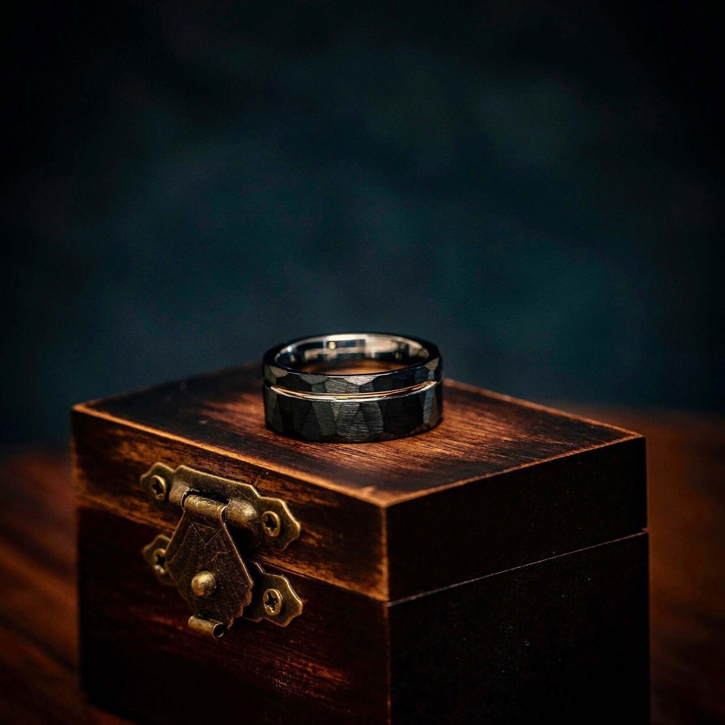 Hammered Black Tungsten Wedding Band with Silver Channel Inlay and Polished Silver Inner Band laying on its side on top of walnut ring box