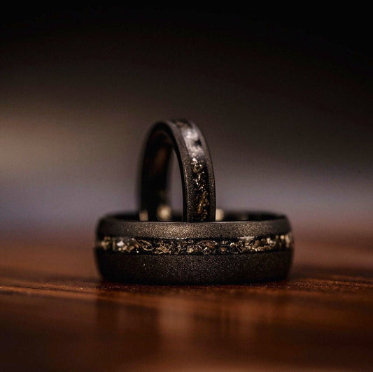 His and hers wedding ring set featuring black sandblasted and meteorite bands, symbolizing unity.