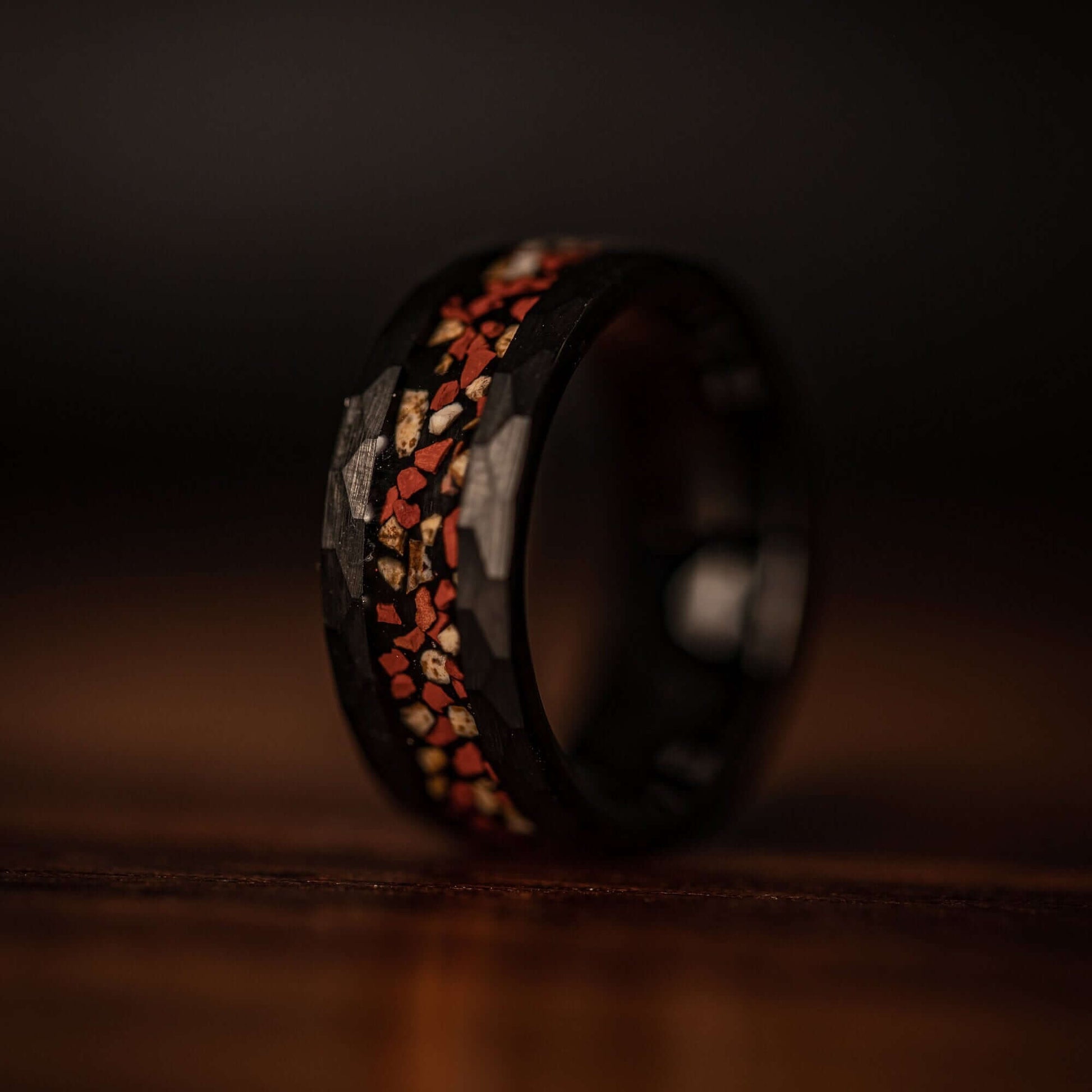 Hammered Black Tungsten Wedding Ring with Red and White Dinosaur Bone Inlay standing on its side