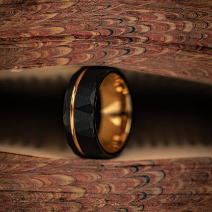 Hammered Black Tungsten Wedding Ring with Polished Rose Gold Inner Band standing on its die between pages of a book
