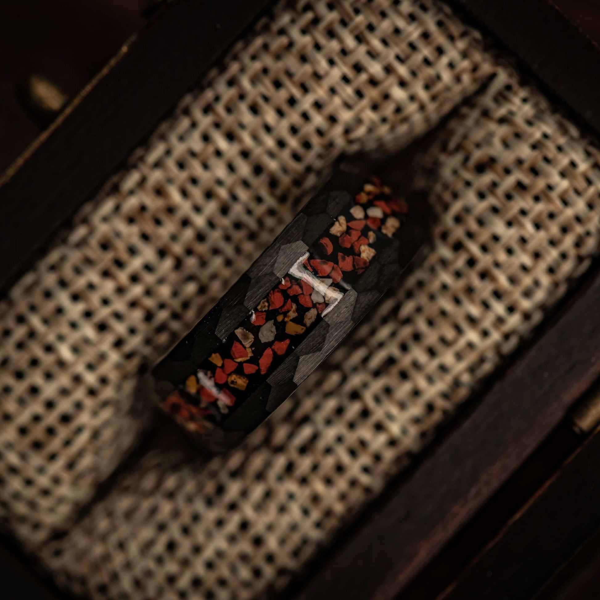 Hammered Black Tungsten Wedding Ring with Red and White Dinosaur Bone Inlay inside walnut ring box between burlap cushions