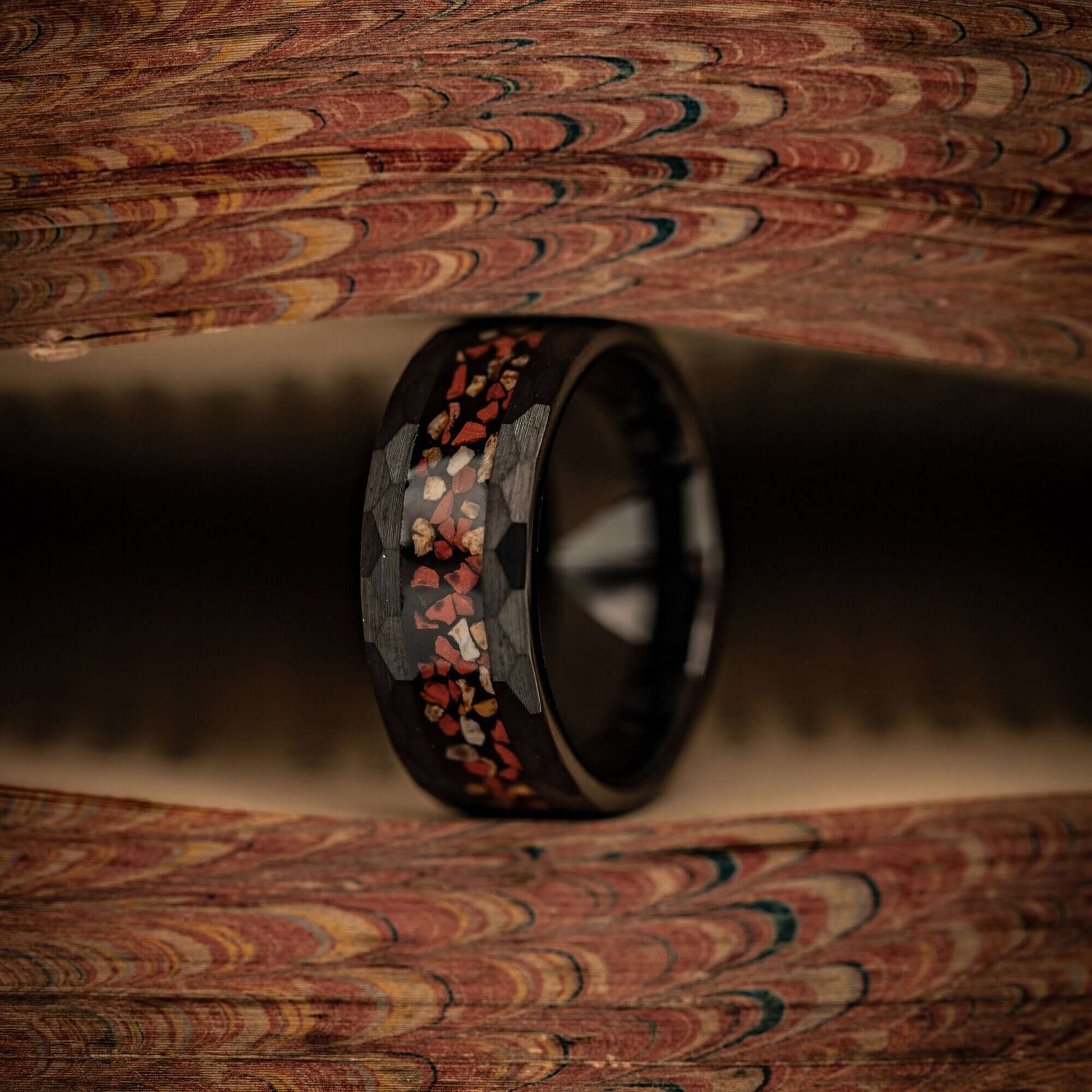 Hammered Black Tungsten Wedding Ring with Red and White Dinosaur Bone Inlay standing on its side between pages of a book