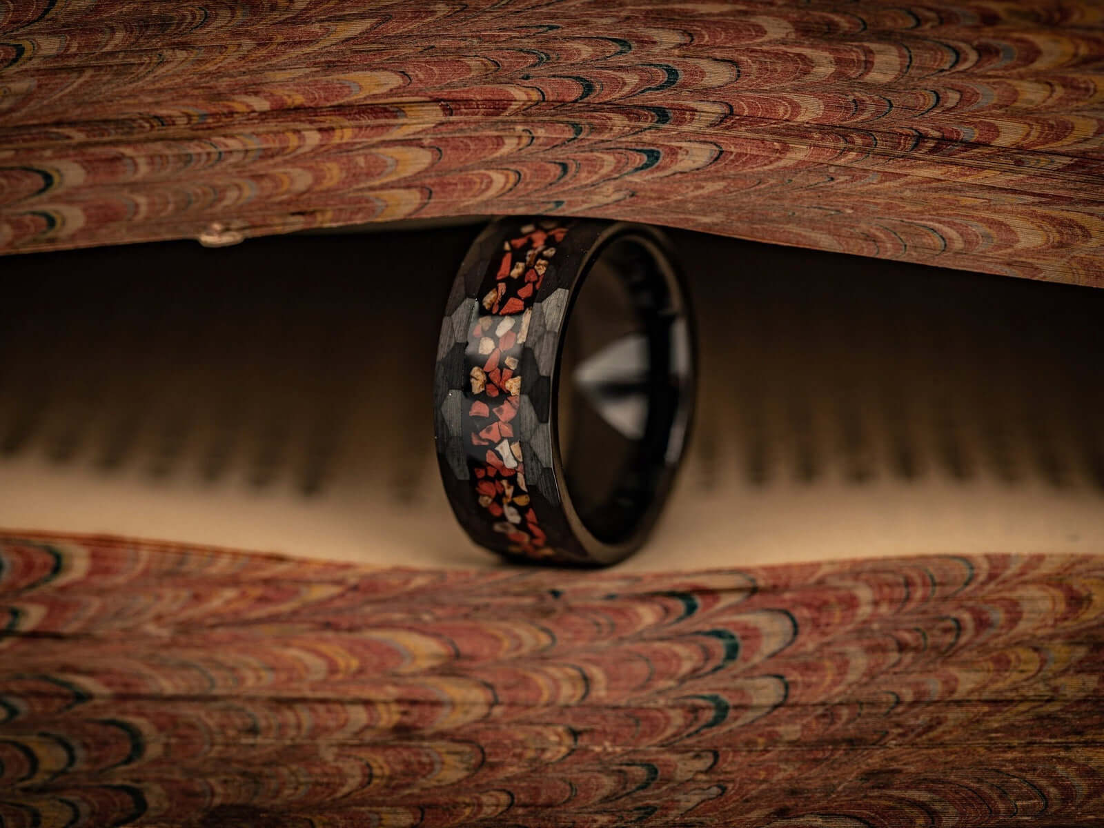 Hammered Black Tungsten Wedding Ring with Red and White Dinosaur Bone Inlay standing on its side between pages of a book