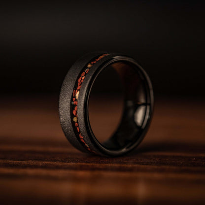 Bold wedding ring featuring black sandblasted tungsten and vivid red dinosaur bone accents.