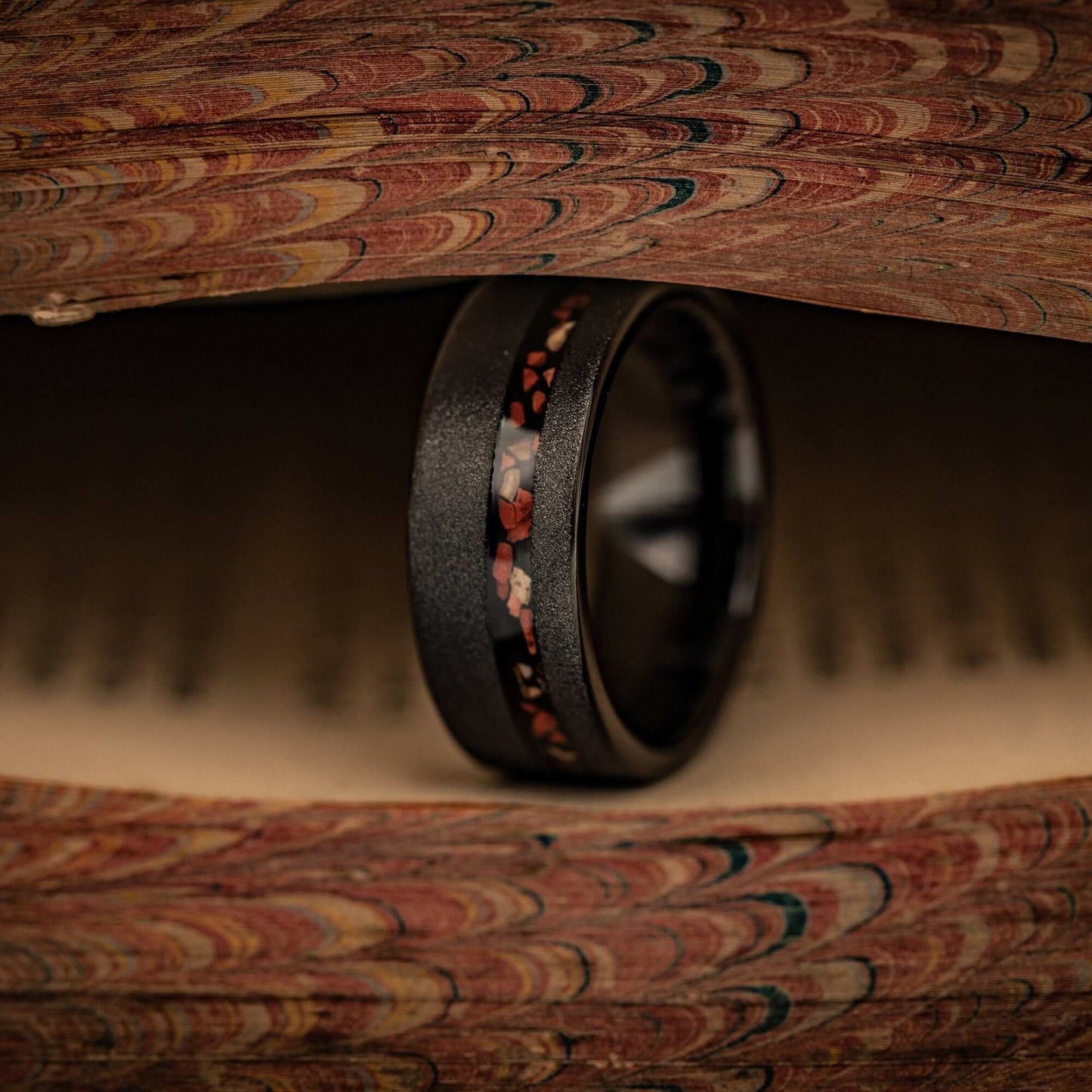 Striking black wedding band with red dinosaur bone inlay, showcasing unique T-Rex bone detailing.