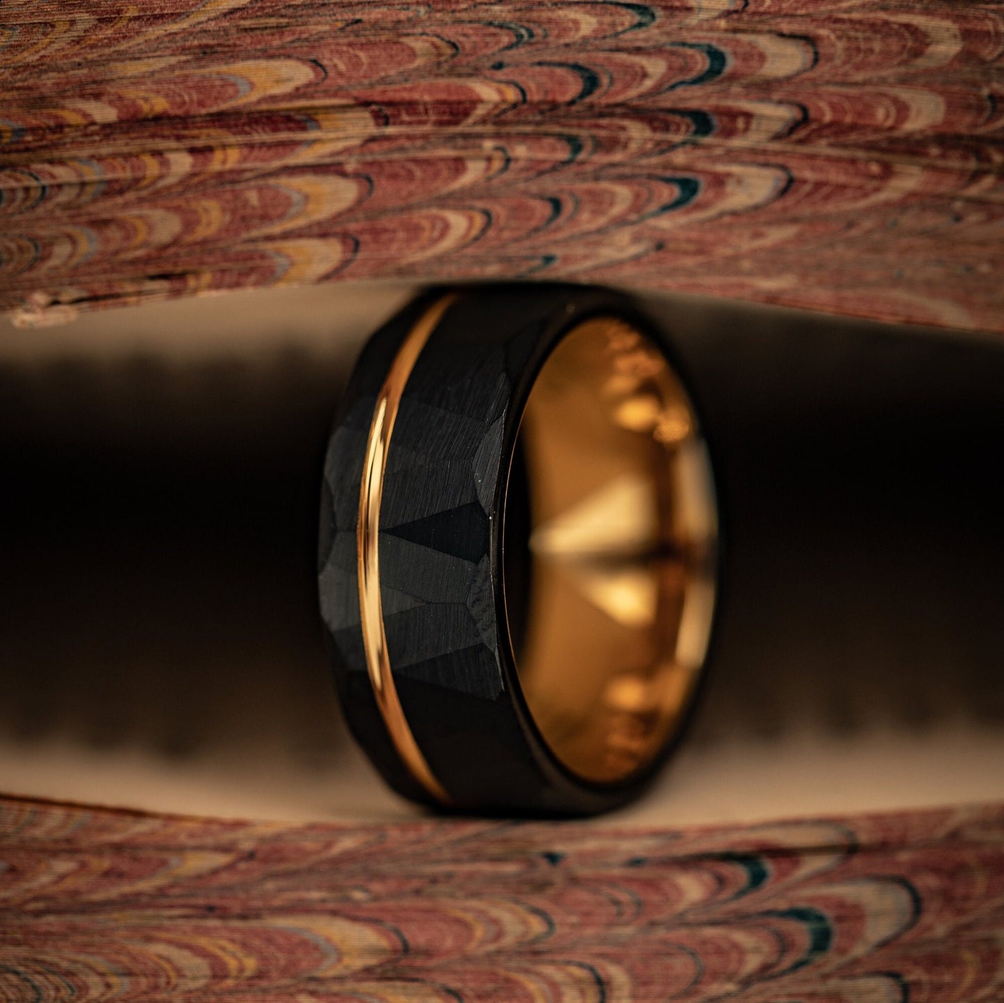 Hammered Black Tungsten Wedding Ring with Polished Rose Gold Inner Band standing on its side between pages of a book