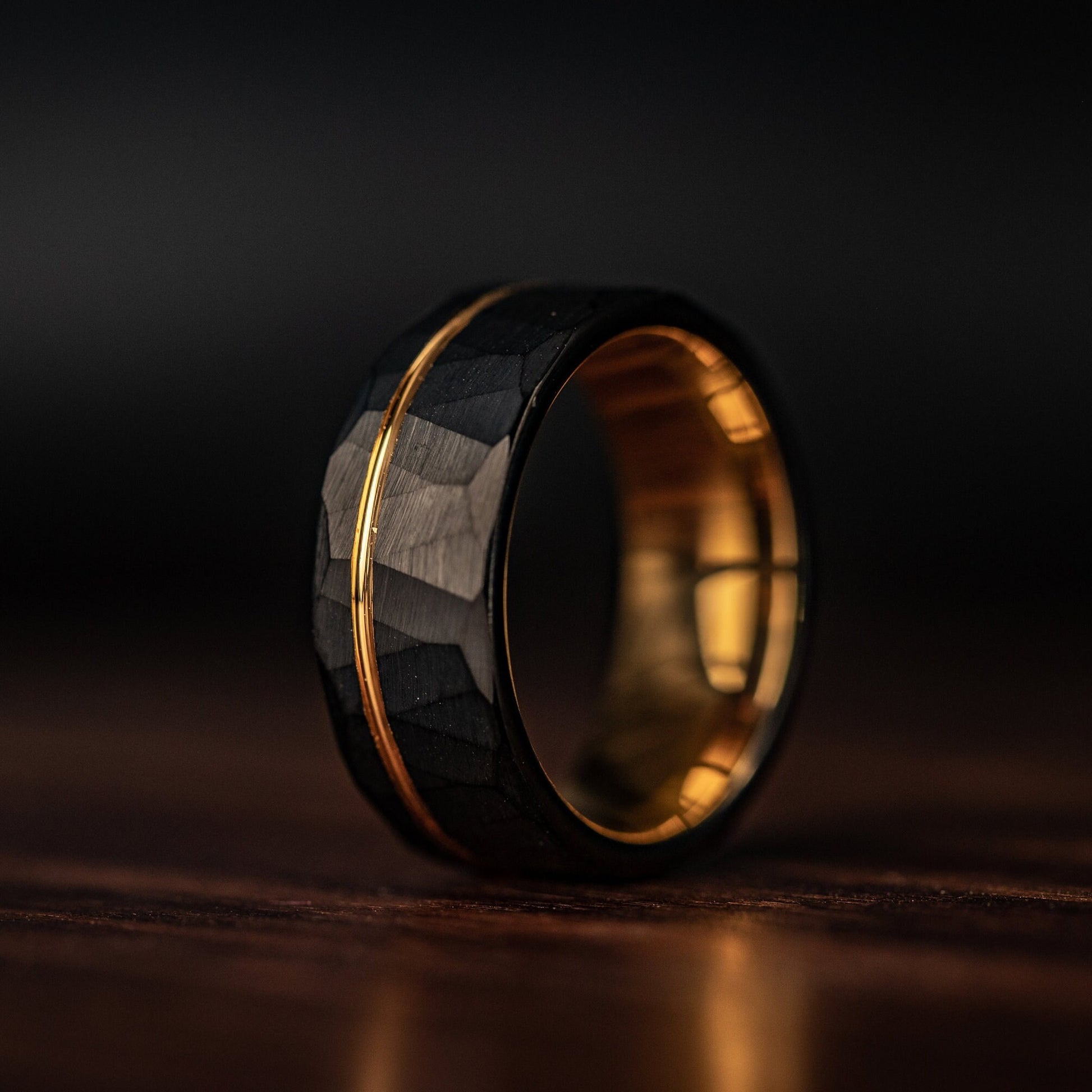 Hammered Black Tungsten Wedding Ring with Polished Rose Gold Inner Band standing on its side 