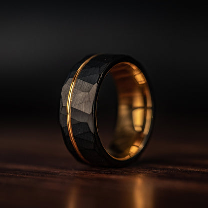 Hammered Black Tungsten Wedding Ring with Polished Rose Gold Inner Band standing on its side 